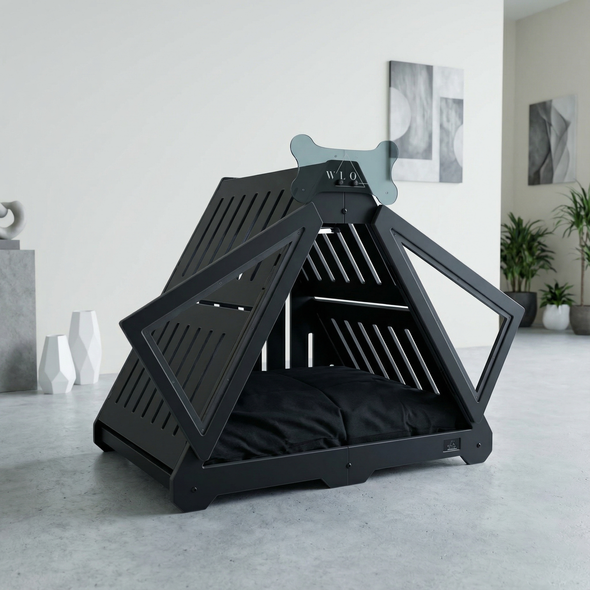 Black pet playpen with cushion on a light gray floor in a room with white walls and decorative plants.